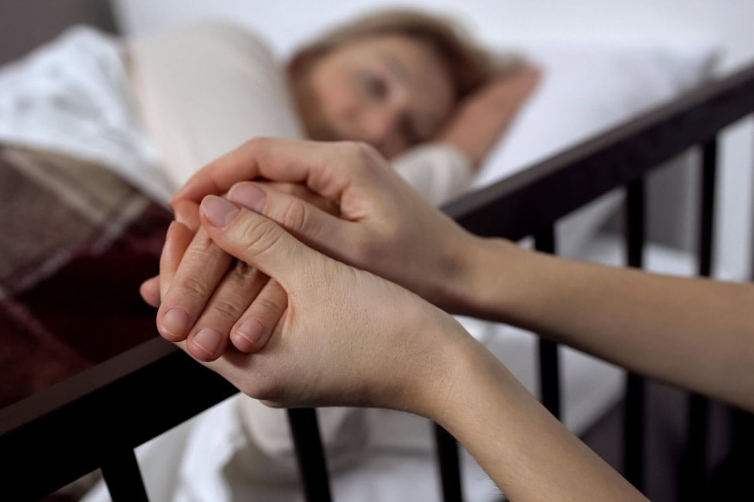 Holding hands of a caregiver and a sick person in bed, symbolises care and support.